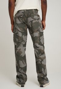 Camo cargo pants in shades of green and gray, featuring multiple side pockets, a relaxed fit, and reinforced stitching.