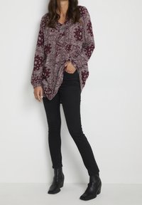 Burgundowa bluzka z długim rękawem w biały wzór paisley, dekolt w kształcie litery V, z bocznymi rozcięciami, połączona z czarnymi skinny jeansami i botkami za kostkę.