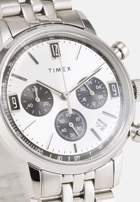 Montre en acier inoxydable argenté avec un cadran blanc, trois sous-cadrans noirs et des aiguilles argentées. Comprend un tachymètre, une fenêtre de date et un bracelet à maillons.