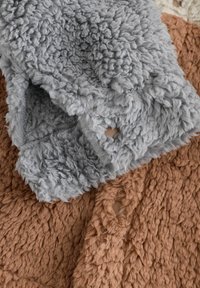 Deux couvertures texturées en gris et marron. La couverture grise présente une surface en boucle, tandis que la marron a une texture shaggy et un trou visible.