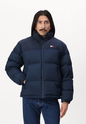 Chaqueta acolchada azul marino con cremallera frontal, cuello alto y un diseño segmentado y acolchado. Tejido texturizado en los hombros con detalle de logo.