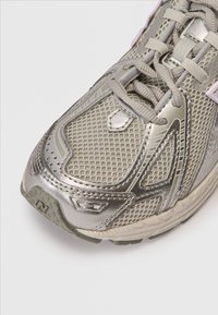 Szara sportowa buty z siateczkową cholewką i metalicznymi srebrnymi akcentami. Charakteryzują się okrągłym noskiem, teksturowanymi powierzchniami oraz widoczną, amortyzującą podeszwą.