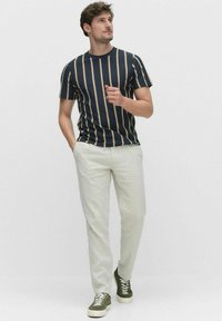 Marine gestreept t-shirt met crème en bruine lijnen, gecombineerd met lichtbeige broek en olijfgroene sneakers. Korte mouwen, ronde halslijn.