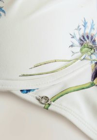 Wit stof met bloemenprints in blauw en groen, met een gladde textuur, gestikte randen en een.detail van een zilveren sluiting.