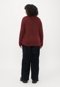Pulover tricotat în nuanță de bordo, cu un model de cusătură deschis, având un gât rotund și mâneci lungi, purtat cu pantaloni negri largi.