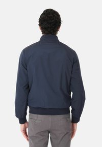 Giacca bomber blu navy con collo a zip e polsini a costine, caratterizzata da un tessuto leggero e liscio e da una vestibilità rilassata.