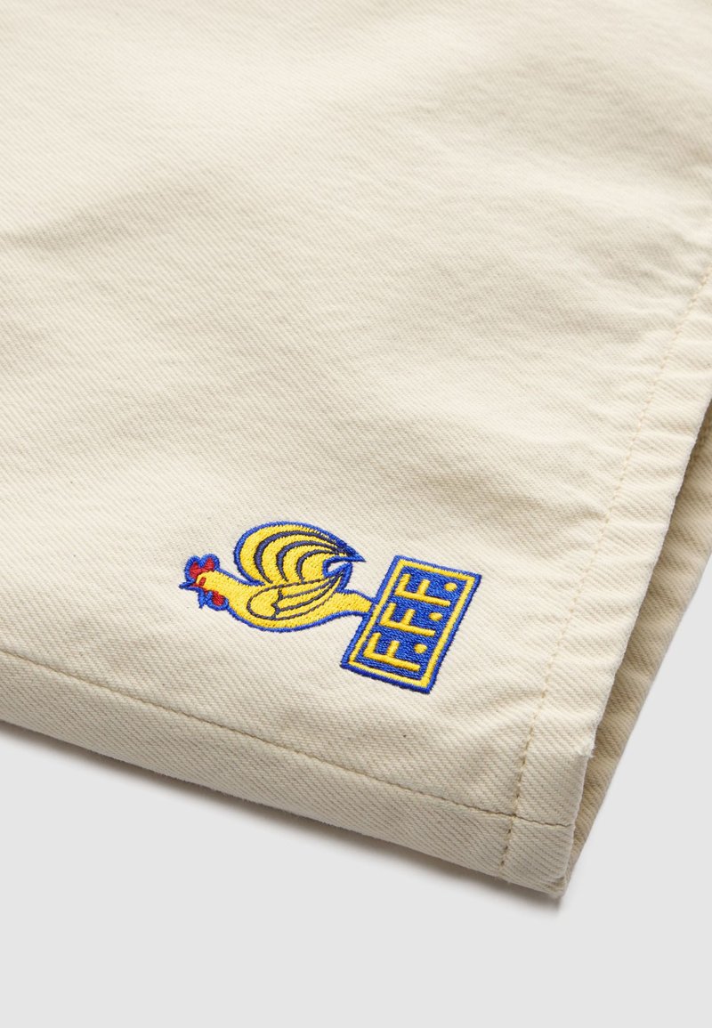 Tessuto beige con un gallo ricamato in giallo sopra un rettangolo blu e giallo contenente le lettere F.F.F.