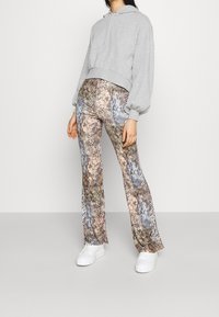 Šedá zkrácená mikina s kapucí a dlouhými rukávy, doplněná rozšířenými kalhotami s hadím vzorem. Celkový vzhled doplňují bílé platformové tenisky.