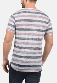 Gestreiftes T-Shirt mit einer Mischung aus Grau, Rot und Weiß. Kurze Ärmel, Rundhalsausschnitt und weicher Stoff mit einer leicht melierten Textur.