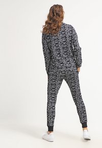 Conjunto de loungewear en blanco y negro con un patrón de formas geométricas, mangas largas y pantalones ajustados con puños negros. Zapatillas blancas.