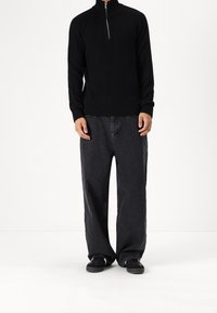 Pull noir côtelé avec un col demi-fermeture éclair, associé à un jean gris foncé ample et des chaussures noires. Design simple et décontracté.