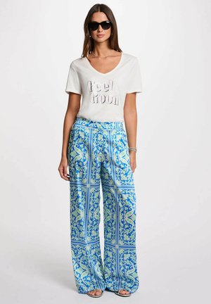 T-shirt bianco con scollo a V con la scritta "Feel Good", abbinato a pantaloni larghi blu con un motivo a fiori verdi e una vestibilità comoda.