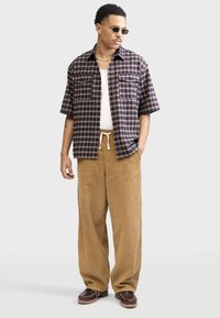 Short-sleeve plaid shirt in navy and tan, paired with beige corduroy pants. Brown shoes with a rugged sole. Visible details include front pockets.