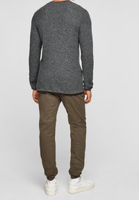 Pull en maille texturée gris foncé à manches longues, associé à un pantalon slim vert olive et des baskets blanches. Détails de poignets ajustés remarqués.
