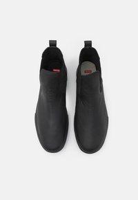 Botas de tobillo de cuero negro con una textura suave, punta redondeada, paneles laterales elásticos y tiradores en el talón para facilitar su uso.