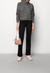 Suéter de cuello alto de punto gris, pantalones acampanados negros, zapatillas de deporte rosa pálido y un pequeño bolso rosa con cadena.