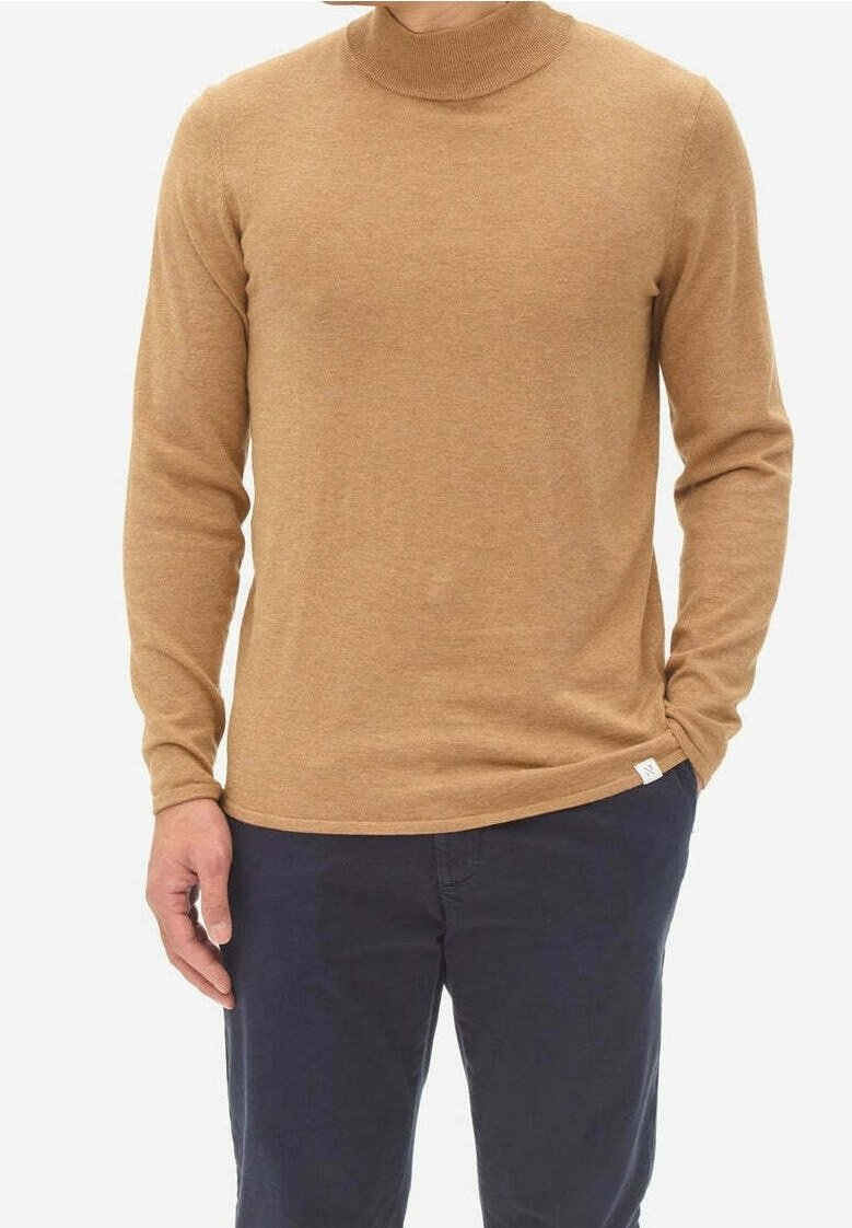 Brown turtleneck sweater in soft knit fabric, featuring long sleeves and a fitted design. Worn over dark pants with a small brand tag visible.