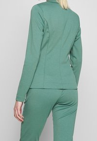 Grön, figursydd blazer i stretchtyg med en mjuk yta. Har en klassisk krage och baksömmar för en skräddarsydd look.