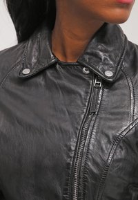 Černá kožená bunda s tlačným límcem, stříbrnými doplňky a šikmým zipem, s hladkým a texturovaným povrchem.
