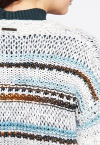 Stickad tröja med en texturerad, vit botten som har blå, bruna och svarta horisontella ränder. Ribbad grön halskrage och logotypdetalj.