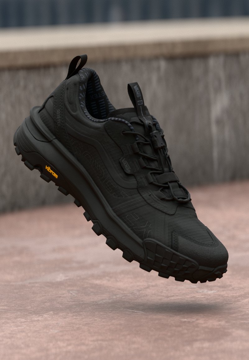 Black, lightweight athletic shoe with mesh upper, rubber sole, and aggressive tread. Features a looped heel tab and subtle branding accents.