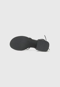 Sandalia negra con suela plana, que presenta una plantilla texturizada y una tira ancha. El diseño es minimalista con una forma simple y recta.