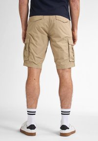 Beige cargoshorts van lichtgewicht stof, met zijzakken en een ontspannen pasvorm, gecombineerd met witte sneakers en gestreepte sokken.