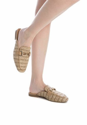 Mules tejidos en beige con un acento de cuero marrón suave y detalles metálicos. Diseño de punta redonda y tacón bajo.
