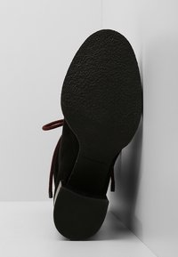 Black suede ankle boot with a textured rubber sole and red laces. The heel is solid and low-profile, with a smooth finish and subtle accents.