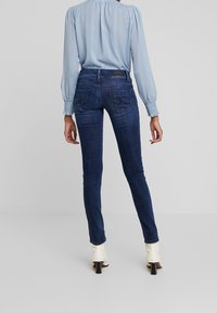 Smal jeans i mörkblå denim, femfickorsdesign, med subtila blekta områden. Matchas med en ljusblå blus med prickar och lång ärm.