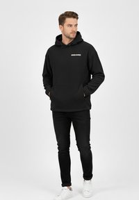 Black hoodie with a front pocket, featuring a white "WORLDWIDE" logo. Paired with black jeans and white sneakers, stands on a neutral background.