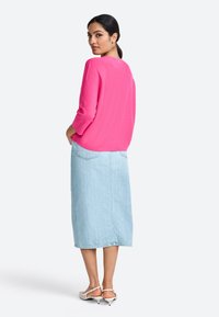 Růžový pletený svetr s tříčtvrtečními rukávy, doplněný světle modrou džínovou midi sukni. Outfit je zjemněn bílými sandály na podpatku.