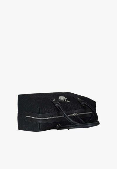 Borsa in pelle nera testurizzata con due manici, cerniera argentata ed emblema decorativo argento sulla parte anteriore, vista da un'angolazione bassa.