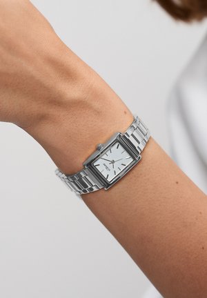 Silberne Armbanduhr mit rechteckigem Zifferblatt, weißem Ziffernblatt, silbernen Stundenmarkierungen und einem Gliederarmband aus Metall. Schlichtes Design und polierte Oberfläche.