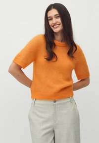 Oranje gebreide trui met korte mouwen en een ronde halslijn, gemaakt van zacht, gewatteerd materiaal, gecombineerd met lichtgrijze, op maat gemaakte broeken.