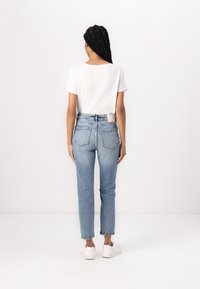 Top blanco de manga corta combinado con jeans de pierna recta de lavado claro que presentan una textura deslavada y bolsillos traseros visibles. Zapatillas blancas.