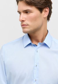 Lichtblauw button-up shirt met een gestructureerde kraag, witte knopen en een decoratief patroon op de binnenkant van de kraag. Gladde stofstructuur.