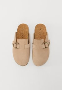 Mocassini beige senza chiusura con una finitura in suede liscia, soletta in sughero e una fascia decorativa con una fibbia tondeggiante dorata.