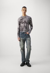 Long-sleeve gray shirt with black graphic print, paired with blue faded jeans and black shoes. Simple design with varied textures.