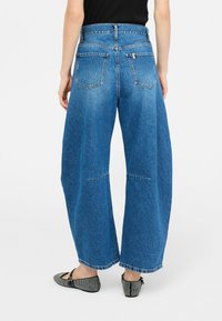 Jeans in denim blu a gamba larga con vita alta, dotati di due tasche posteriori e orlo pulito. Indossati con scarpe basse nere.