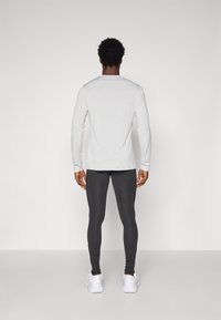 Maglietta grigia chiara a maniche lunghe abbinata a leggings grigi scuri e sneakers bianche, vista da dietro. Design semplice, silhouette aderente.