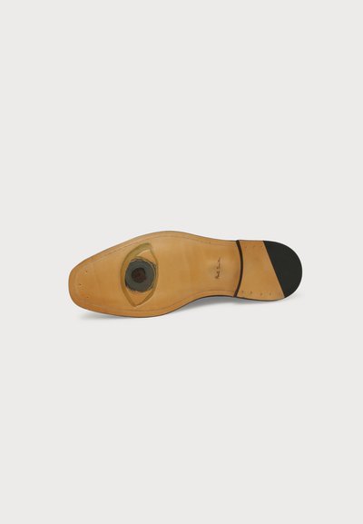 Semelle de chaussure en cuir avec un talon noir et un détail peint d’un œil près de la plante du pied, montrant la signature "Paul Smith".