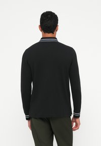 Melnas garām piedurknēm polo krekls ar baltām svītrām ap kaklu un piedurknēm, ar taisnu apakšmalu un mīkstu, teksturētu audumu.