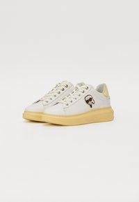 Weiße Leder-Sneaker mit gelber Sohle, ausgestattet mit einem seitlichen Logo und runden Schnürsenkeln. Glatte Textur mit minimalen Mustern und Akzenten.