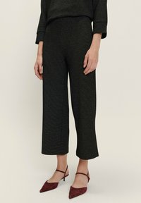 Pantalons noirs raccourcis en tissu texturé, présentant une coupe droite et une taille mi-haute. Associés à des escarpins bordeaux à bout pointu.