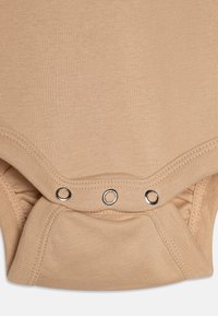 Beige bodysuit i mjukt tyg med korta ärmar, försedd med silverfärgade tryckknappar längst ner och en slät, strukturerad yta.