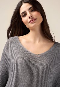 Grauer Strickpullover mit weitem V-Ausschnitt, der ein strukturiertes Muster und eine lockere Passform aufweist, und aus einem weichen, leichten Stoff gefertigt ist.
