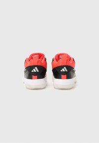 Ein Paar schwarze und orange Adidas-Sneaker mit weißen Sohlen, von hinten auf einem schlichten hellen Hintergrund betrachtet.