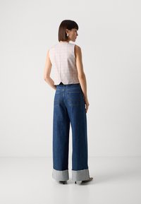 Top fără mâneci, cu carouri roz, având o deschidere la spate, asortat cu blugi lejeri din denim albastru, cu o margine destrămată de culoare gri deschis și buzunare în spate.