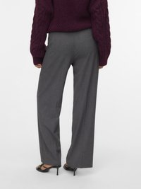 Sive široke hlače z ožjim krojem, narejene iz teksturirane tkanine. Kombinirane z grobim bordovim puloverjem z vzorcem kable in črnimi sandalami s peto.